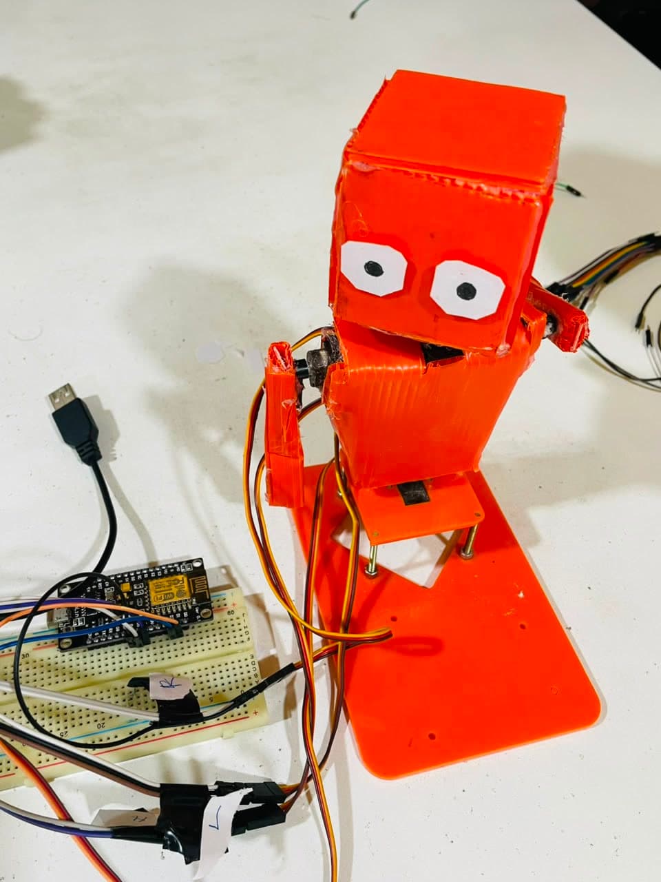 An orange 3D-printed servo robot built in the workshop, wired to a NodeMCU board