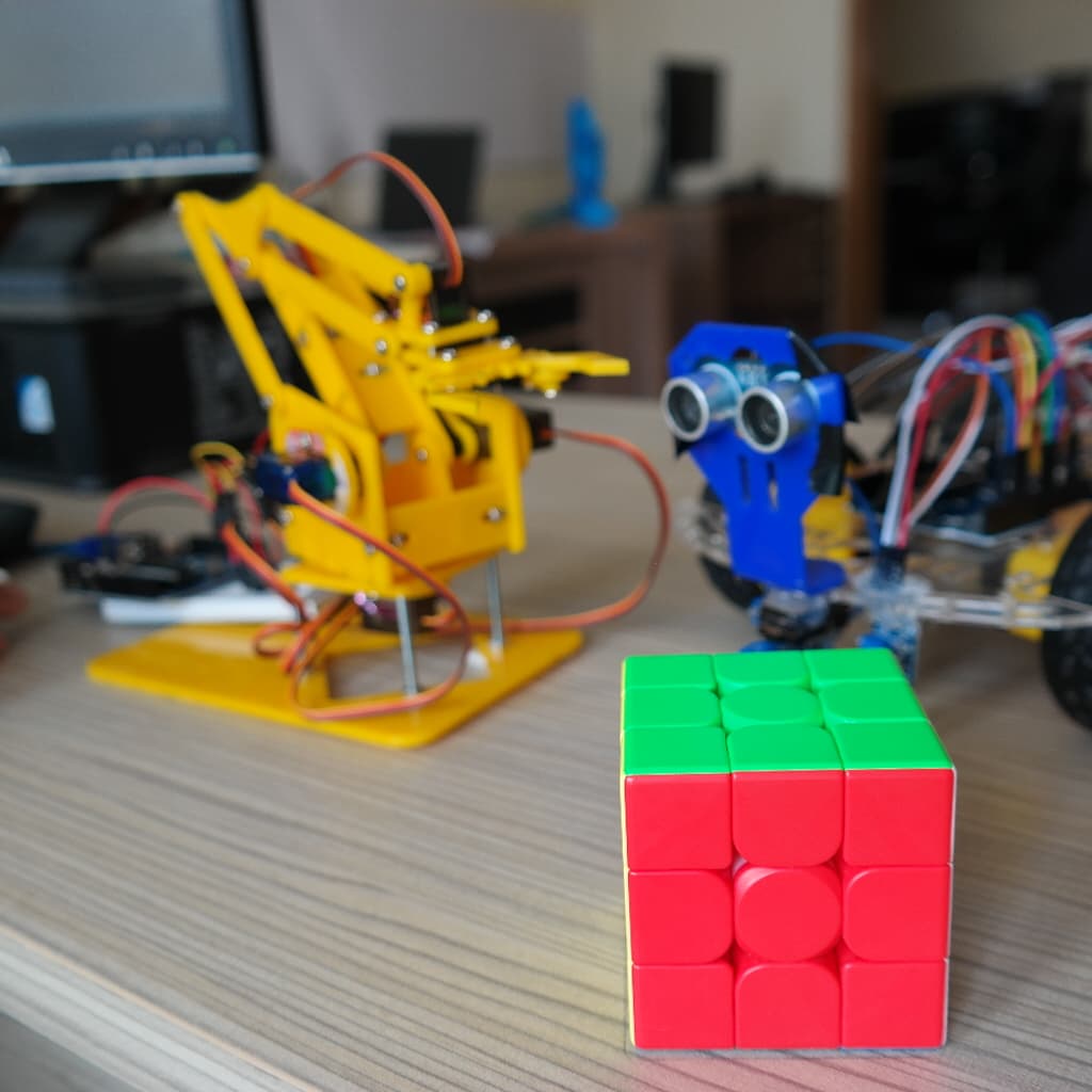 A student-built robot arm beside a sensor rover and a Rubik's cube